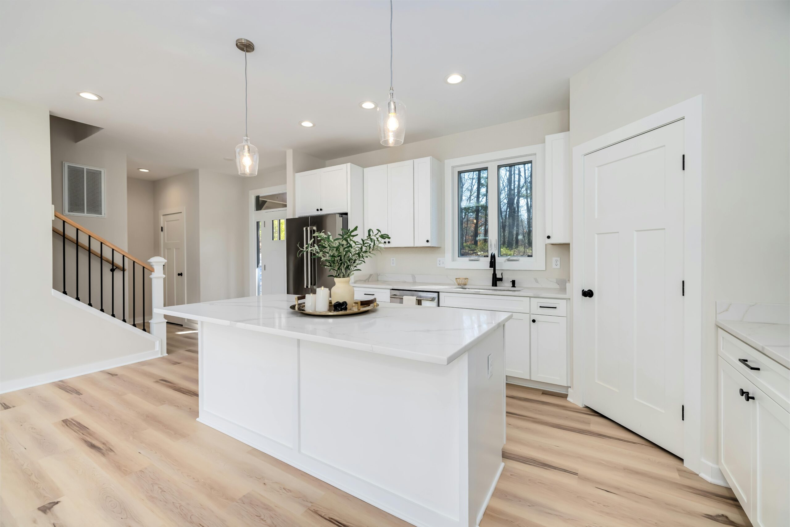 Bright modern kitchen featuring white cabinets and island, with minimalist decor.